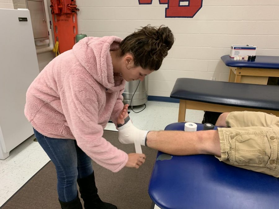 Ashlee McQuon taping the ankle of football player, Kayden Grubbs.