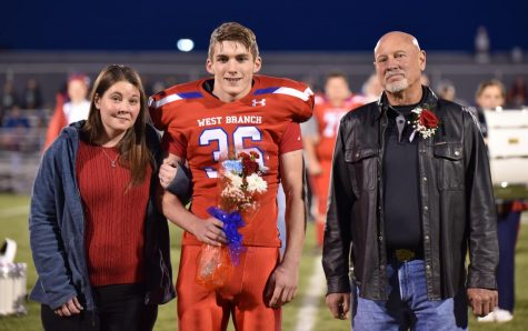 Aidan Kephart walking down the field on senior night escorted by his mom and grandfather.