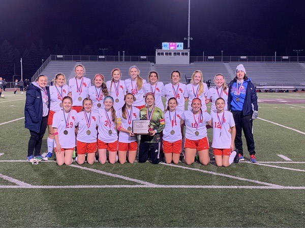The Lady Warrior Soccer team smiles for a photo as captains Sarah Betts and Trinity Prestash hold the second consecutive District 6 title