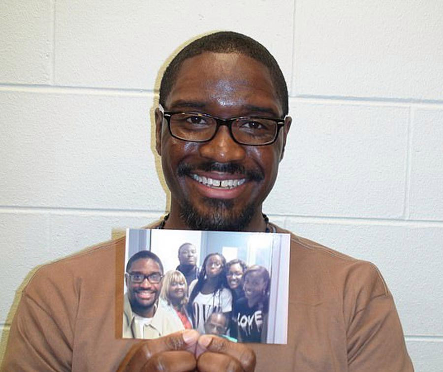 Brandon Bernard smiling while holding up a picture of his family.