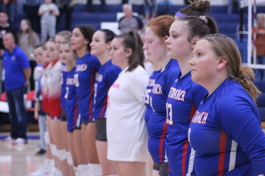 The volleyball team stands together for the playing of the national anthem.