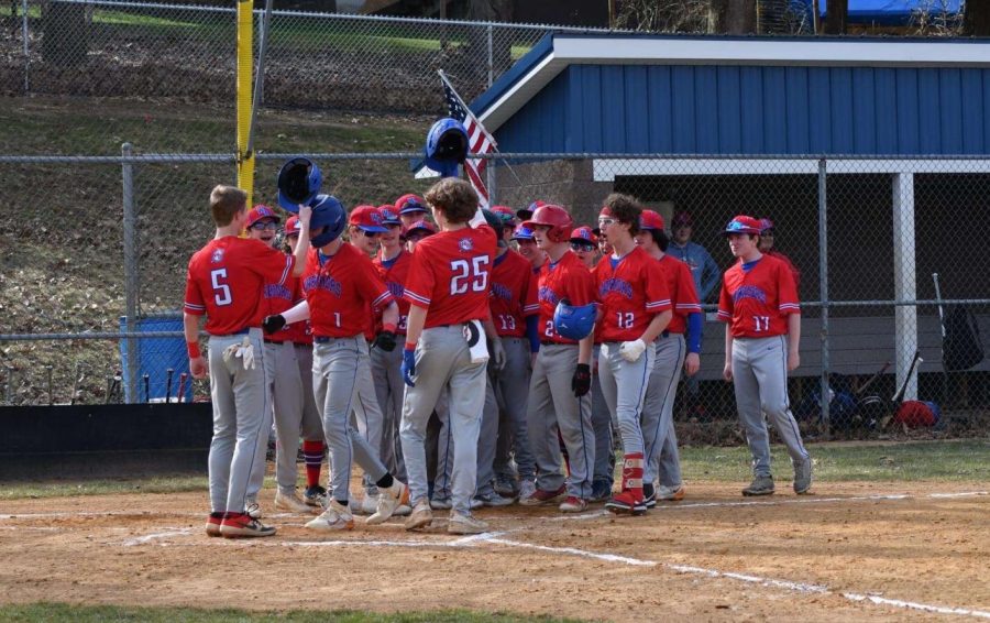 The baseball team surrounds Lukas Colton at home plate after he hits a home run against Harmony.