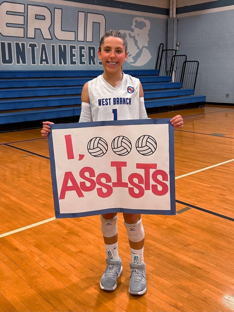 Kyla smiles big holding her 1,000 assist sign.
