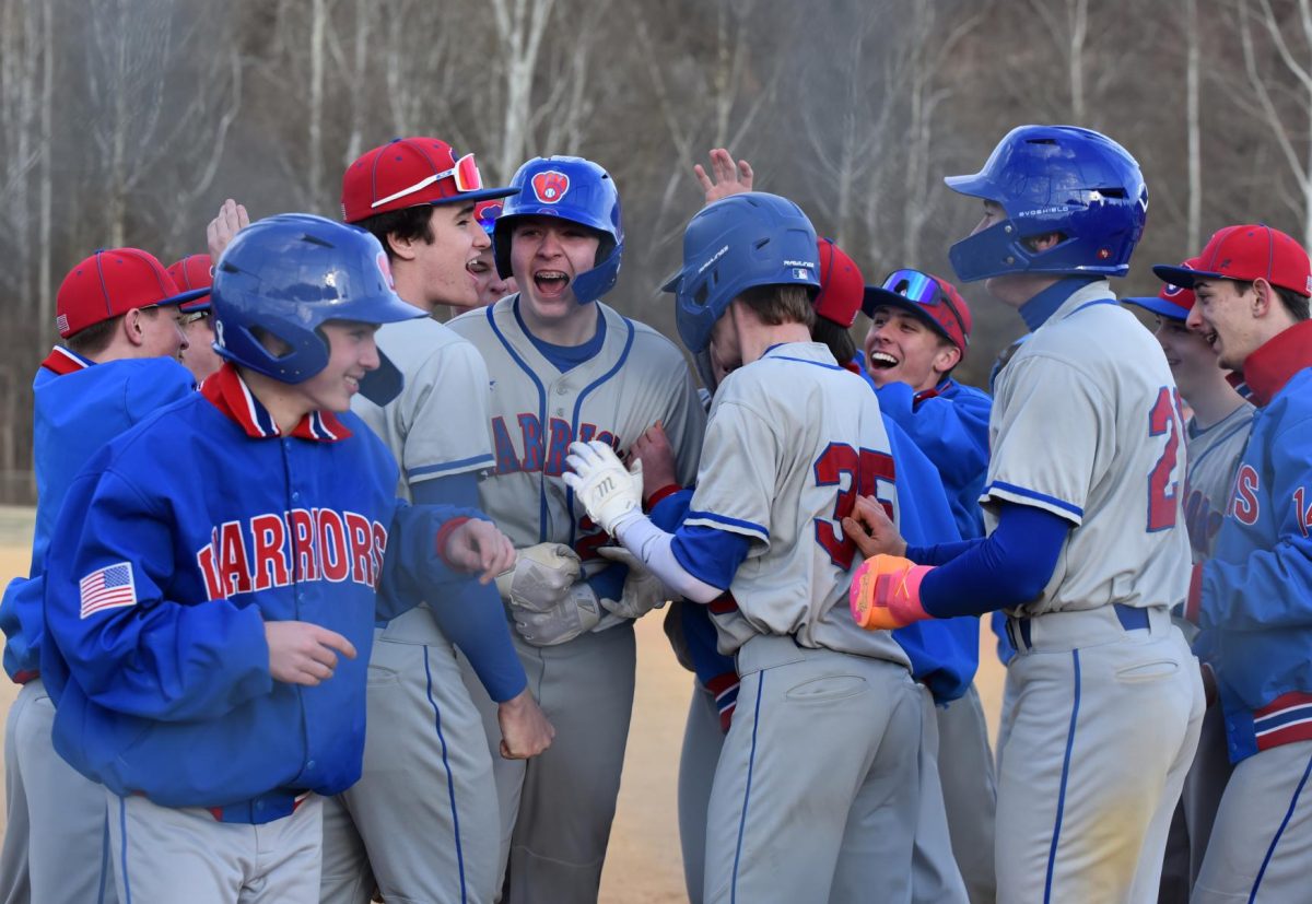 Caleb Hudson and his teammates rally around him as he steps on home plate after hitting a home run.