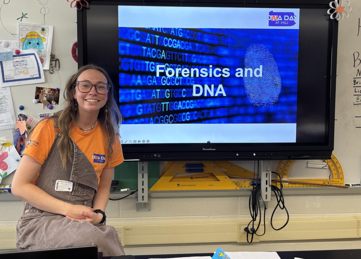 A Penn State graduate school student poses by her presentation in Mrs. Emigh’s room.